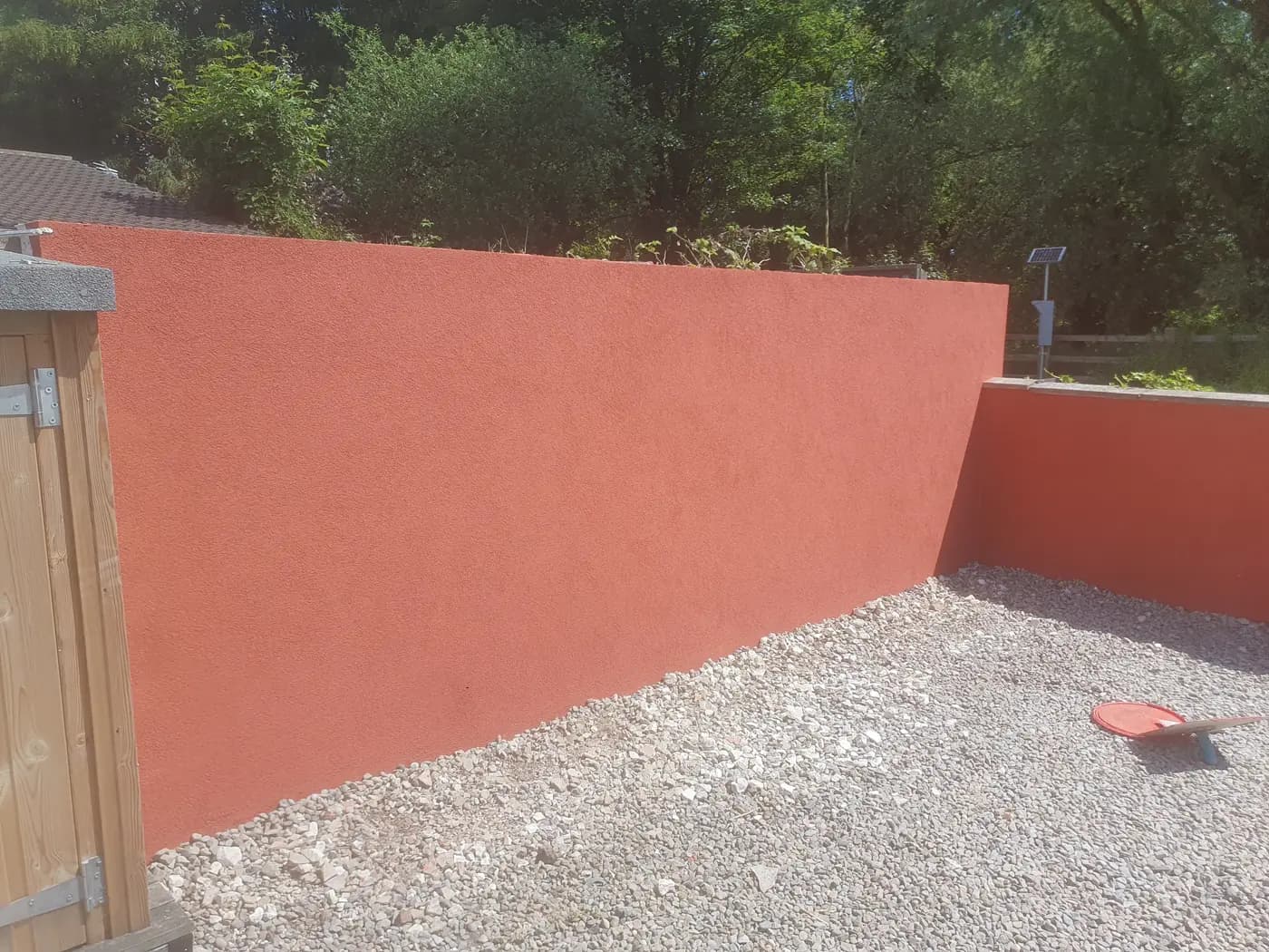 Garden boundary wall rendered in terracotta silicone — bold colour, even texture
